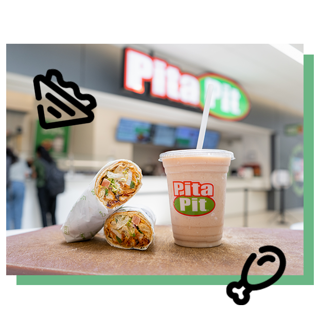 Two wraps and a shake on the table with pita pit store in the back