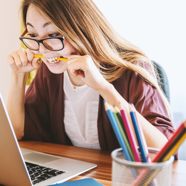 A girl biting a pencil in front of a laptop